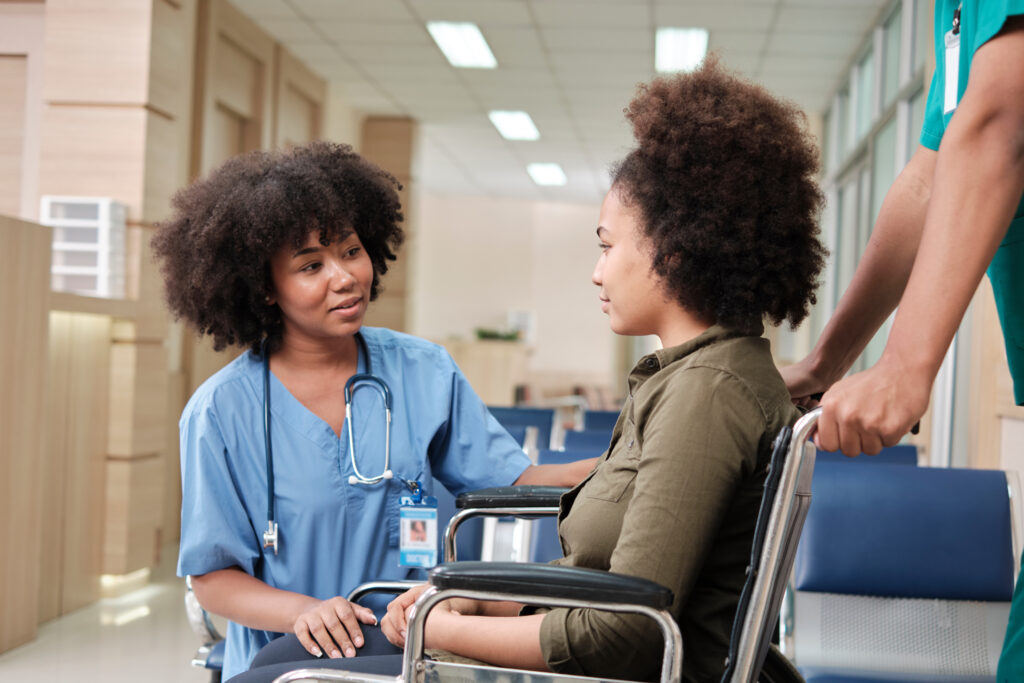 African American female doctor checks patient girl in wheelchair at hospital.