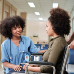 African American female doctor checks patient girl in wheelchair at hospital.