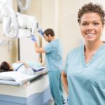 Portrait of radiologist smiling while colleague preparing patient for xray in examination room