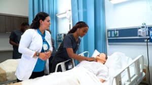 A nurse is standing over a patient laying in a hospital bed, the patient has an oxygen mask on and has other tubes and wires hooked up to him