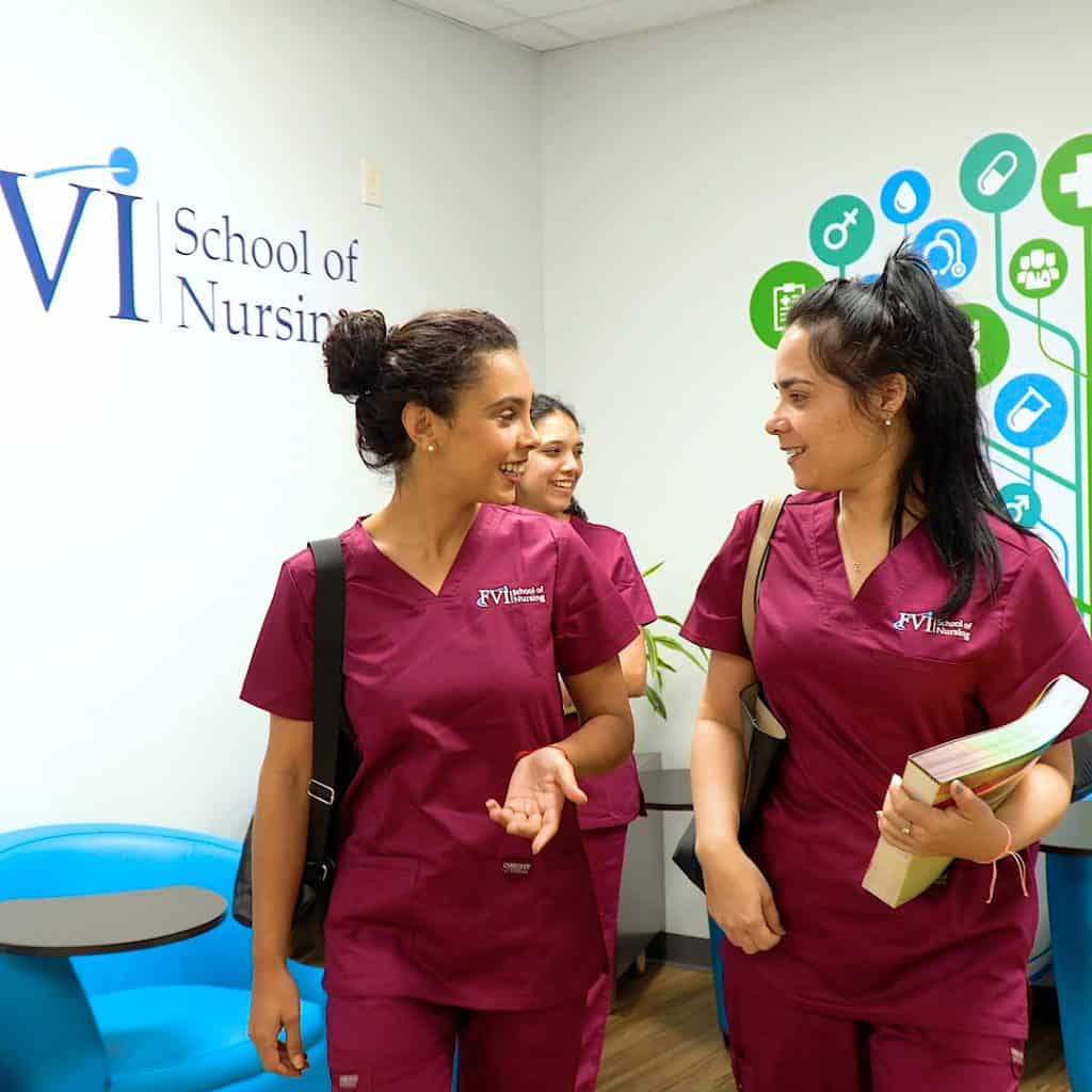 Three Practical Nursing students smiling and talking at FVI School of Nursing, wearing burgundy uniforms.